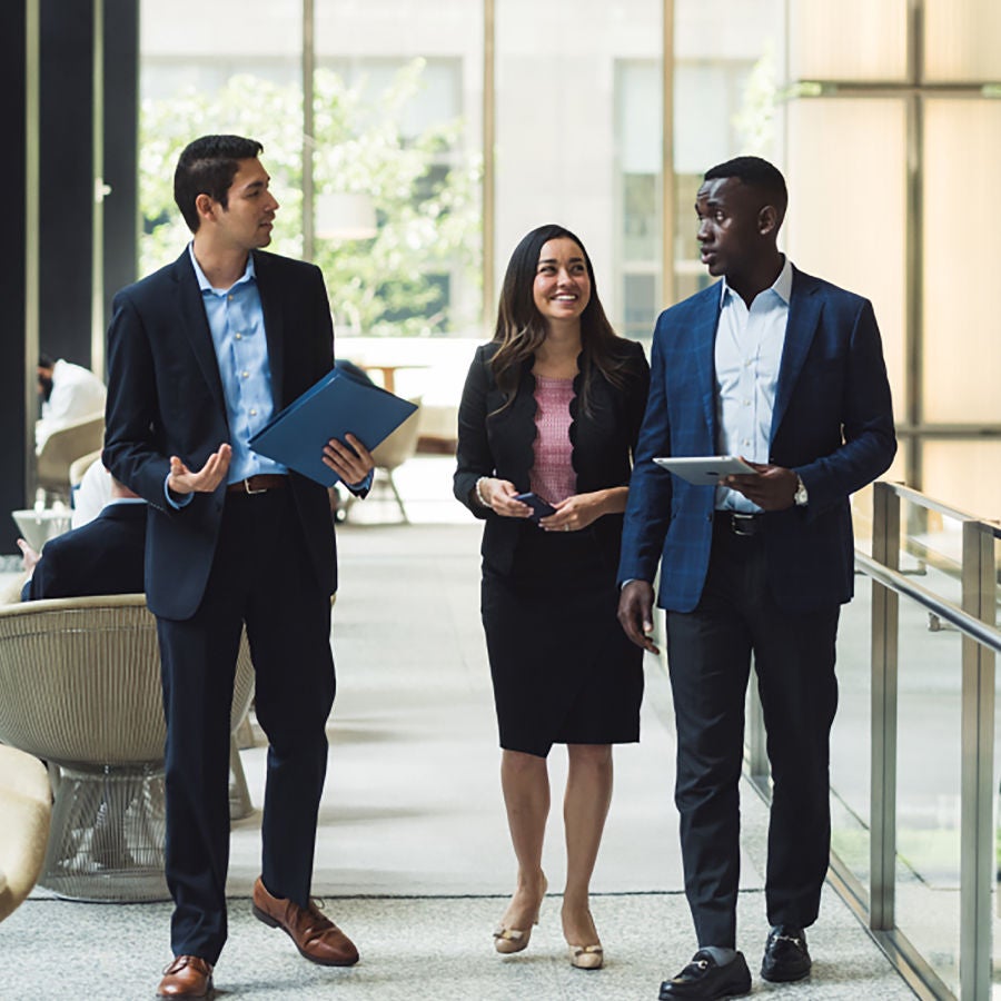 Three business professionals engaged in conversation in a modern lobby setting.
