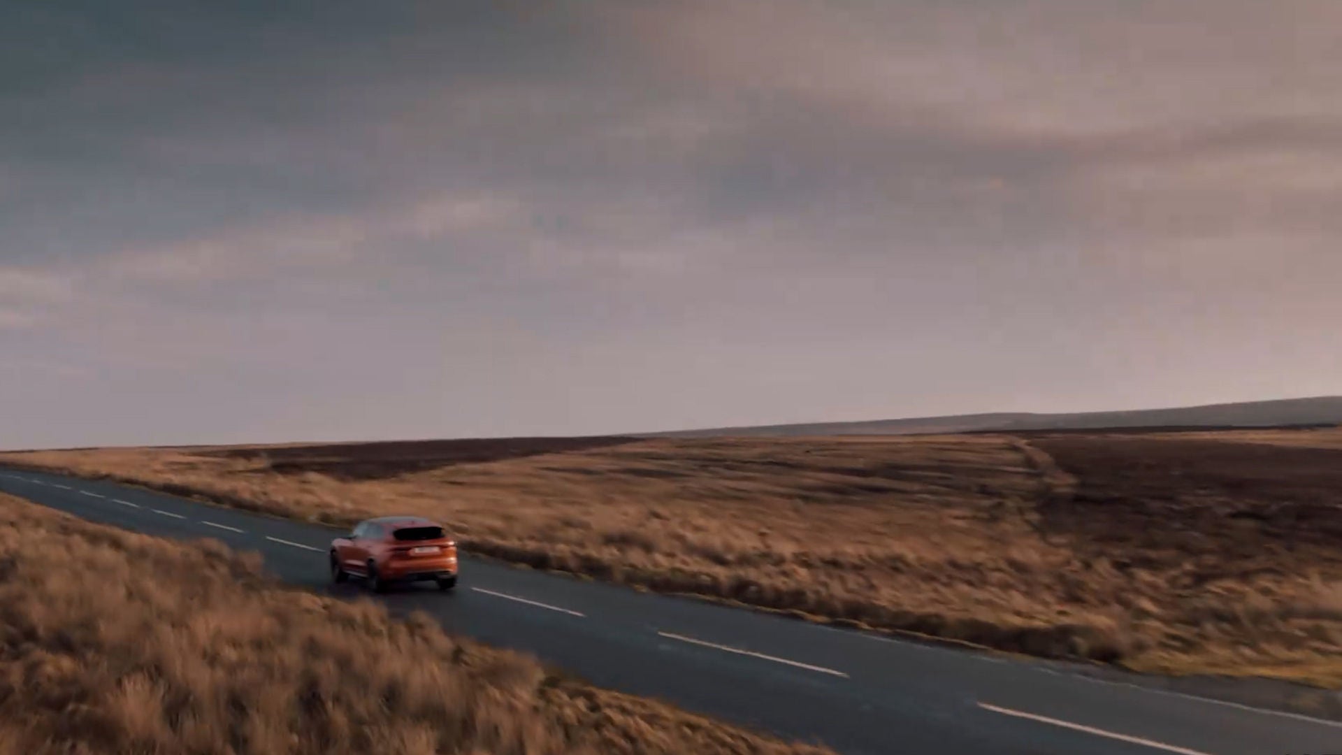 A vehicle drives along a rural road through an open landscape.
