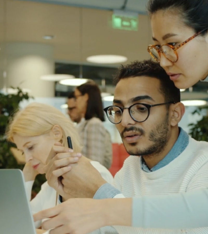 Two professionals collaborating in a modern office space, focused on a laptop screen, discussing and analyzing data.