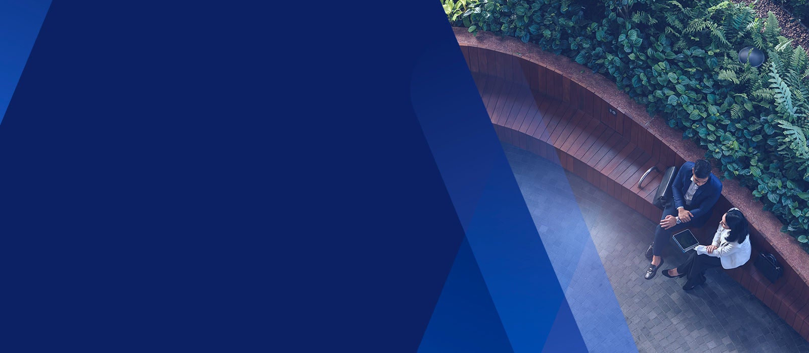 A man and women sitting on a bench outside looking down at a tablet. 