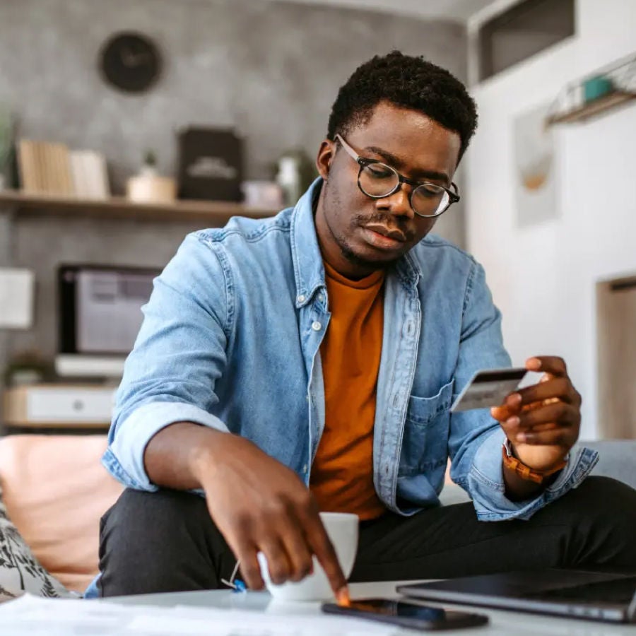 A man using a laptop at home, holding a credit card, illustrating the concept of online payments or shopping.