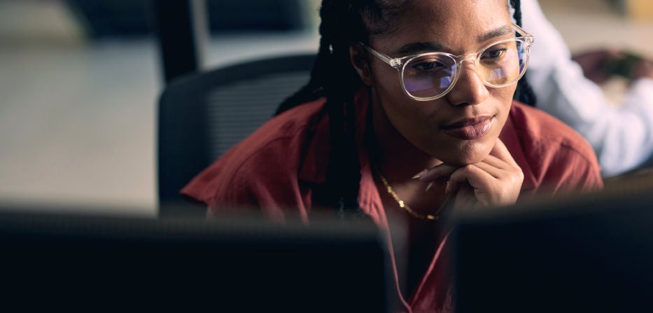 Close-up of a woman wearing glasses, focused intently on a computer screen in an office setting.