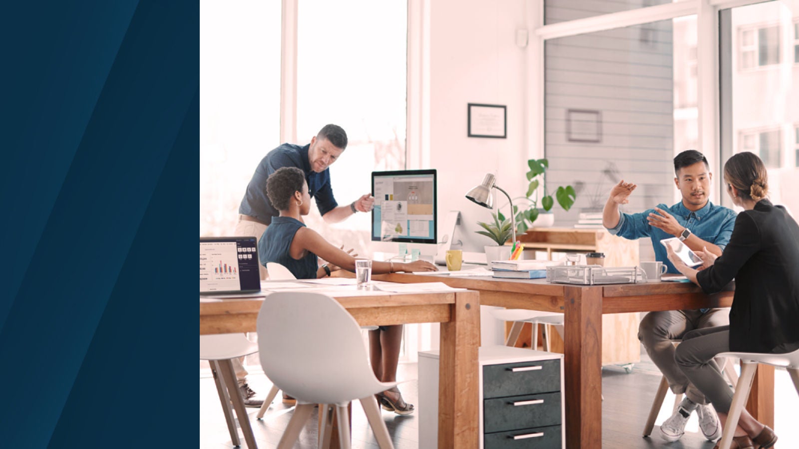 The image shows a collaborative office setting with four colleagues working together, reviewing data on screens and tablets, representing technology-driven planning.