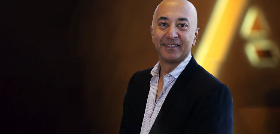 Professional headshot of a man in a suit standing in front of a blurred background with the Anaplan logo faintly visible.