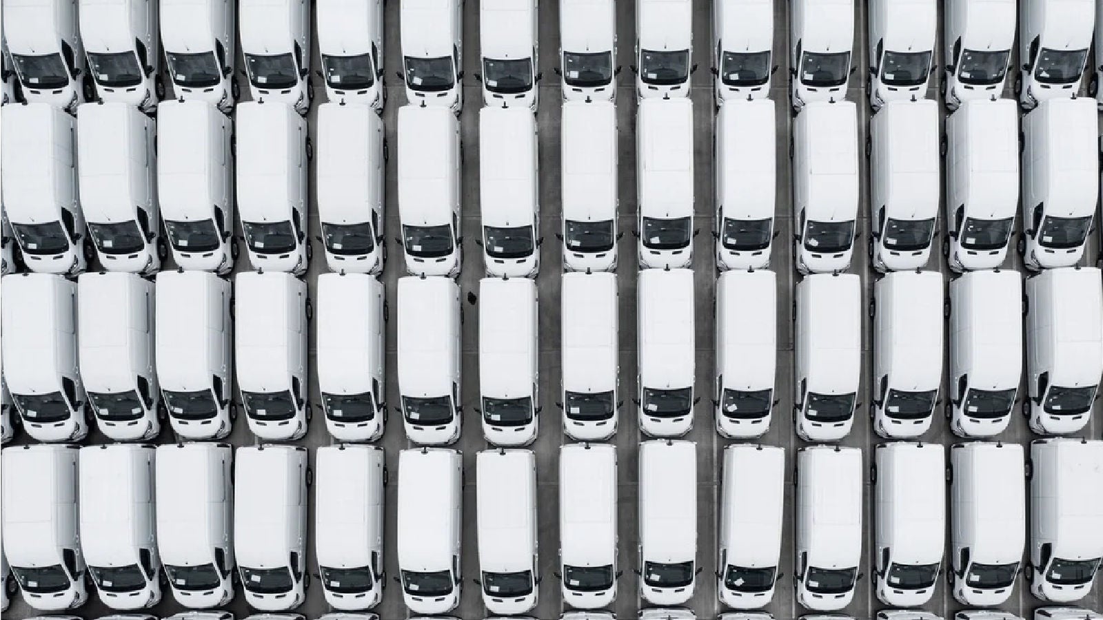 Overhead view of a large, tightly packed fleet of identical white vans parked in rows in a lot.