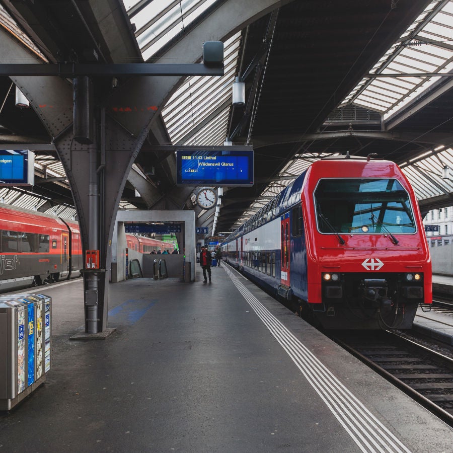 A modern Swiss Federal Railways (SBB) train stationed at a contemporary train platform with digital signage and passengers boarding, representing efficient European public transport.