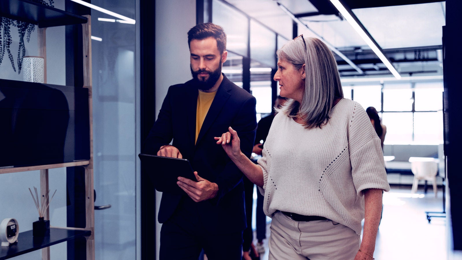two people talking while walking down an office hallway