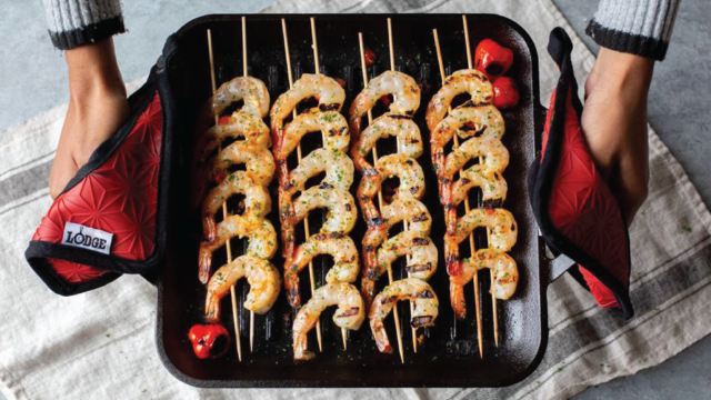 Person holding cast iron cookware with skewered shrimp