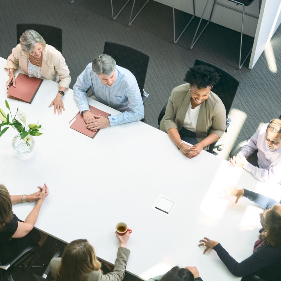 A diverse group of individuals engaged in conversation while seated around a table in a collaborative setting.
