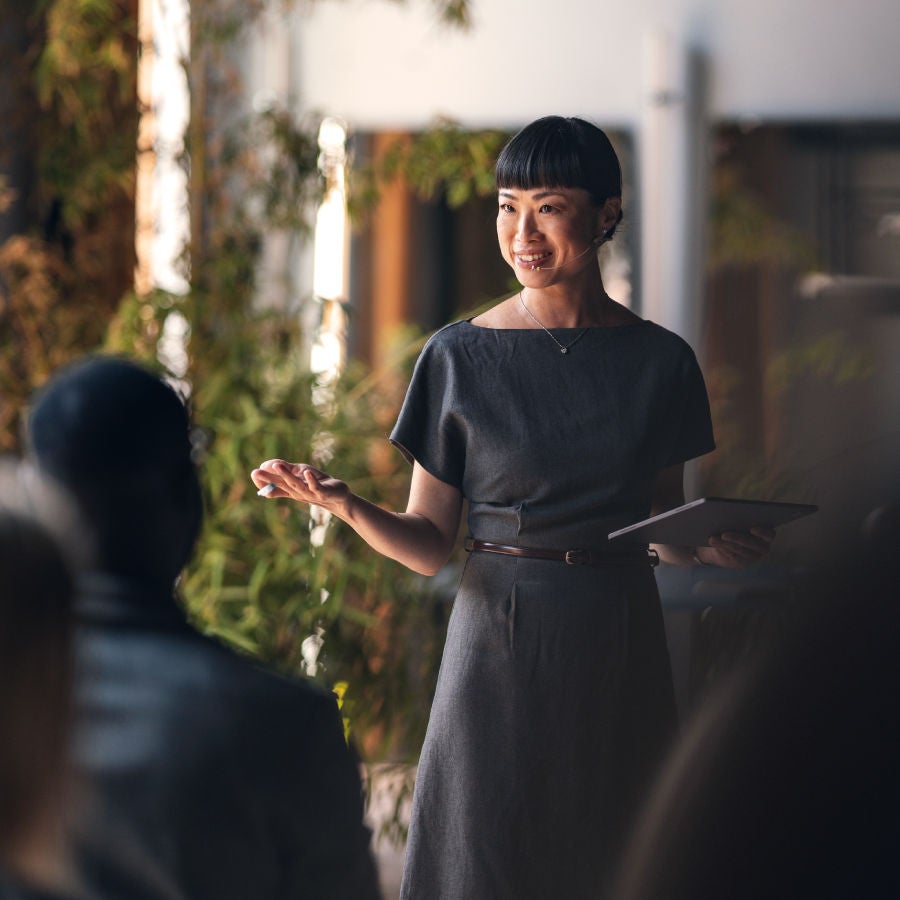 A woman presents to an audience, engaging them with her speech and visual aids in a professional setting.