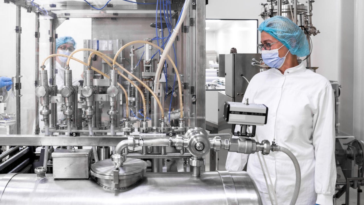 Female worker in protective suit observing lab equipment