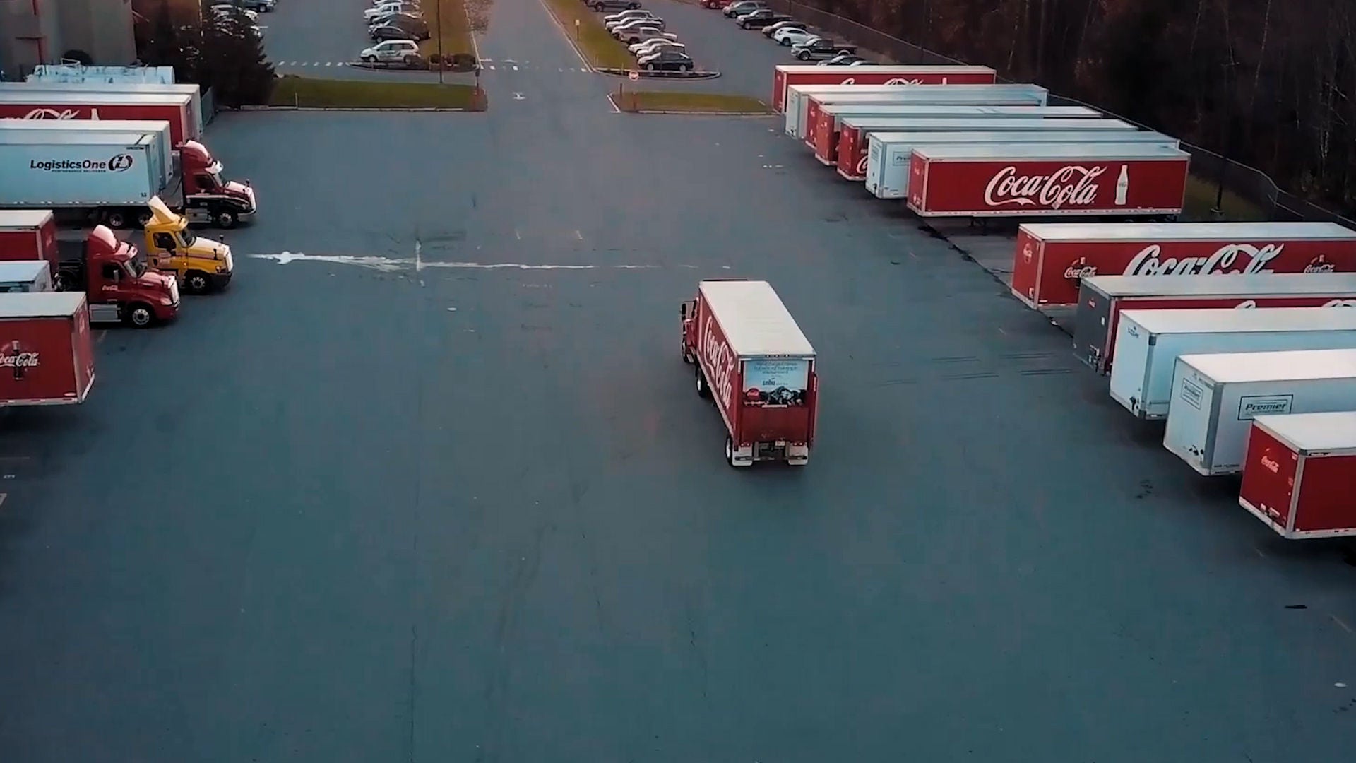 Coca-Cola branded delivery trucks and trailers are parked in a distribution yard.