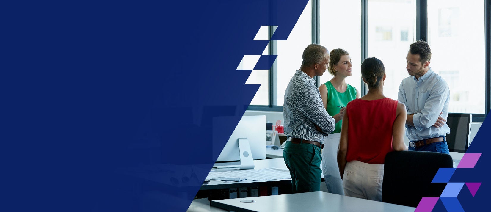 Four coworkers standing in office talking and smiling