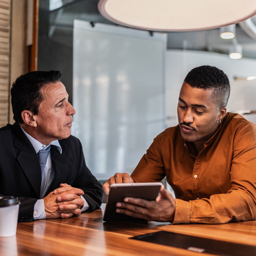 Two men at a table, focused on a tablet screen, engaged in discussion.