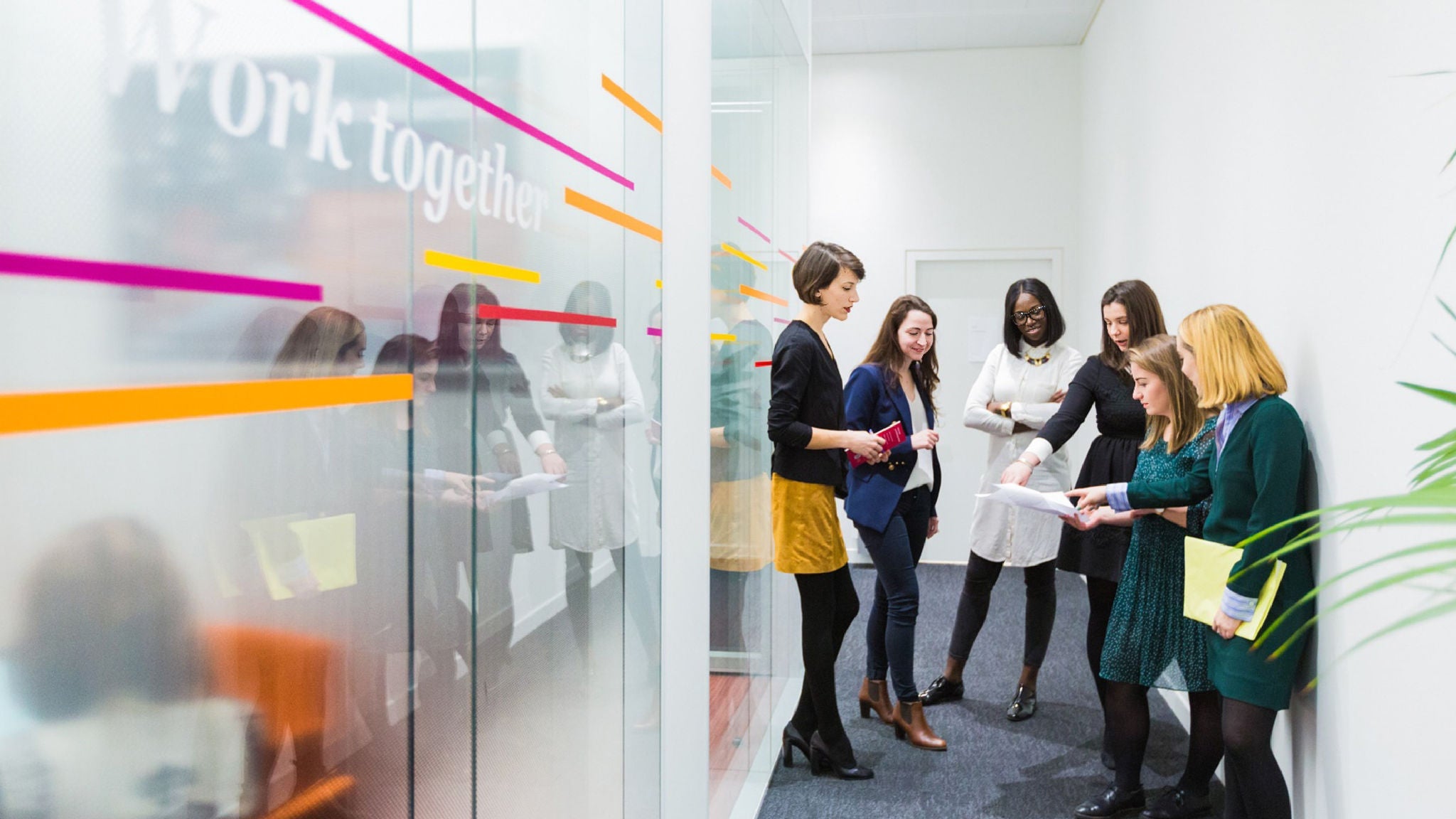 A family doing laundry together in a bright, modern home. A father holds a laundry basket while two children load clothes into a washing machine.