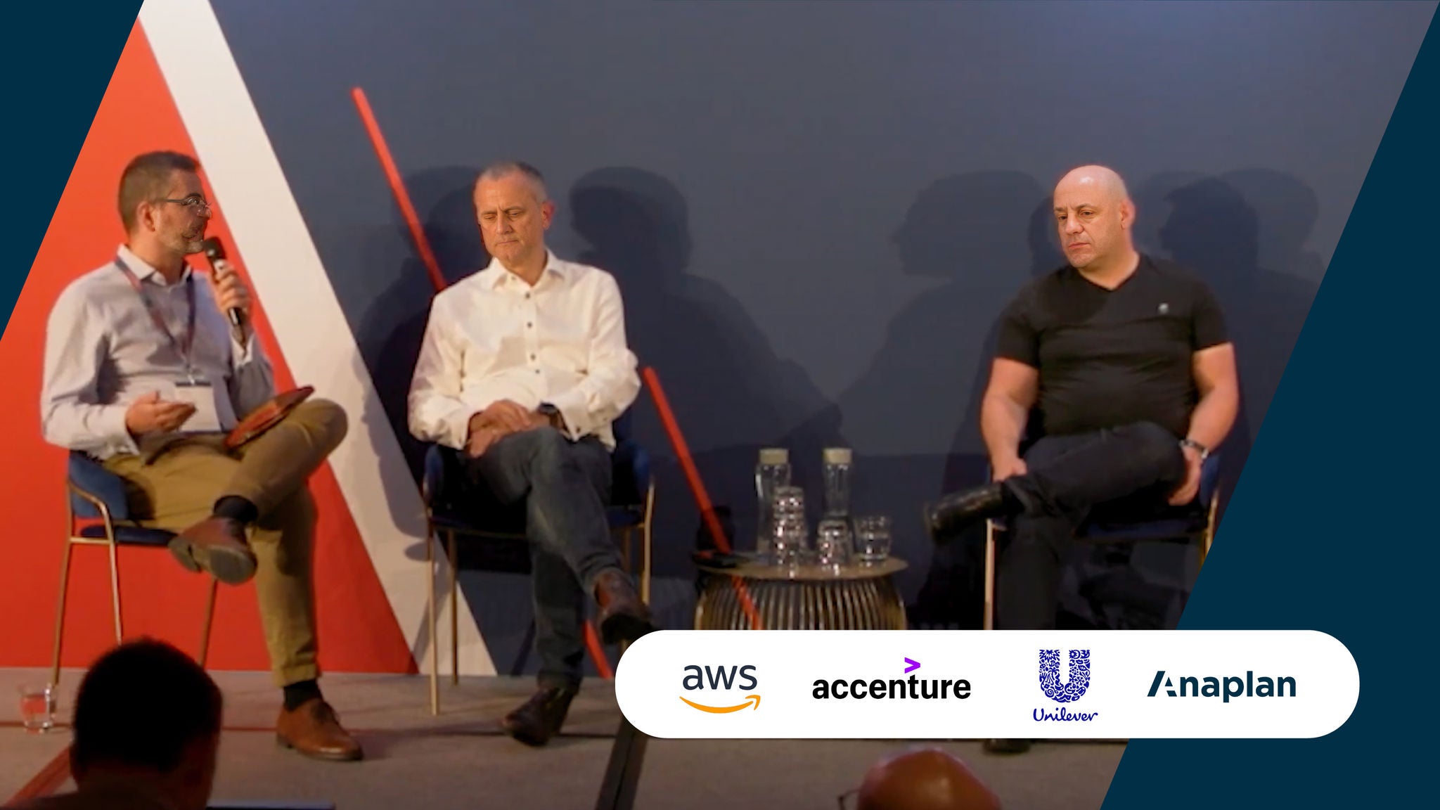 AWS, Accenture, Unilever, and Anaplan Logos displayed bottom right. Three men seated on stage participate in a panel discussion with a microphone and water glasses visible.