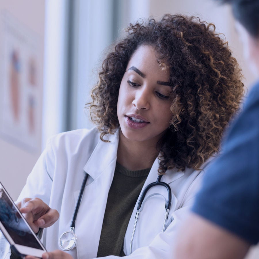 A woman in a doctor's coat examines a tablet, showcasing her engagement with medical technology.