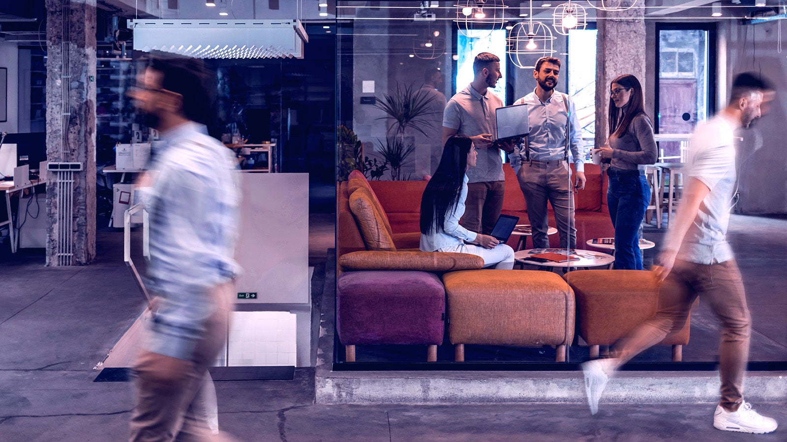 Two men walking outside a glass window with a group of team meeting inside
