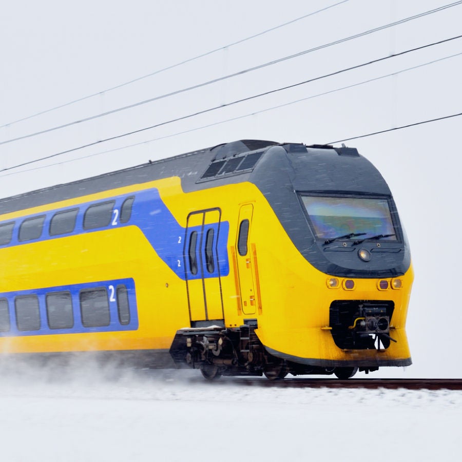 A bright yellow and blue Nederlandse Spoorwegen (NS) double-decker train speeding through snowy conditions, showcasing efficient railway transport in the Netherlands.