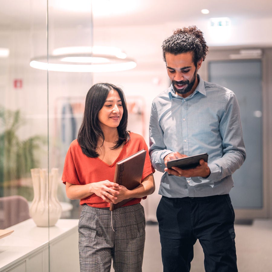 A man and woman standing together in a modern office environment, engaged in conversation.