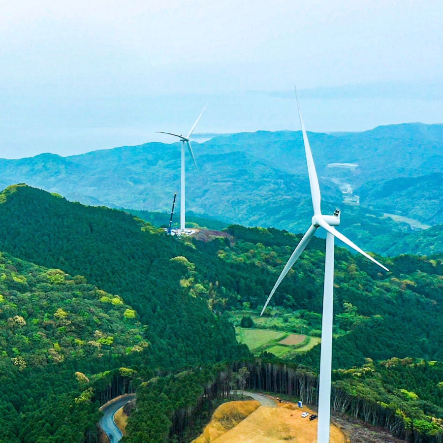 A scenic view of multiple wind turbines standing tall on a green hillside under a clear blue sky.