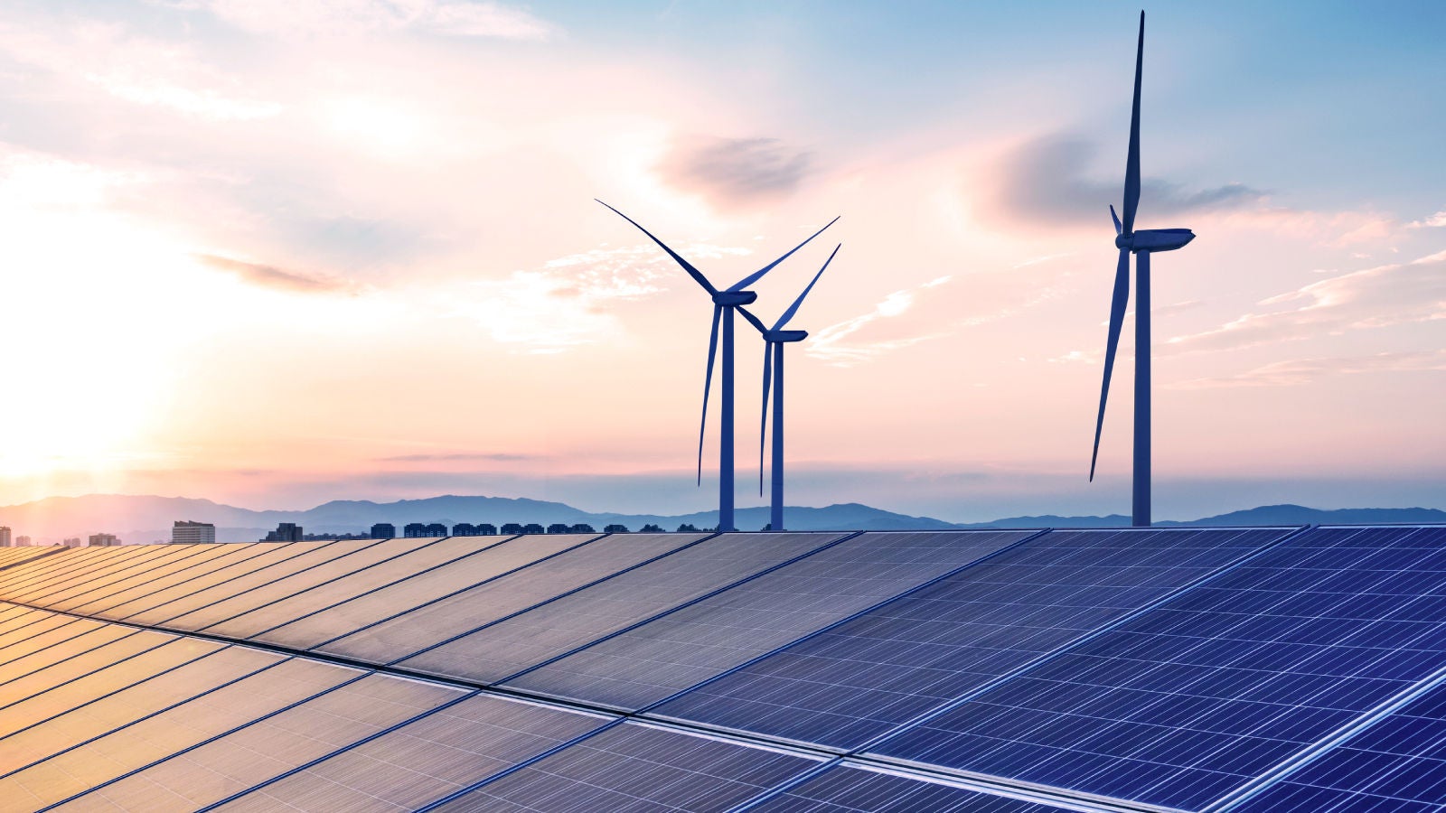 Solar panels and wind turbines under a colorful sunset sky, representing clean energy and sustainability.