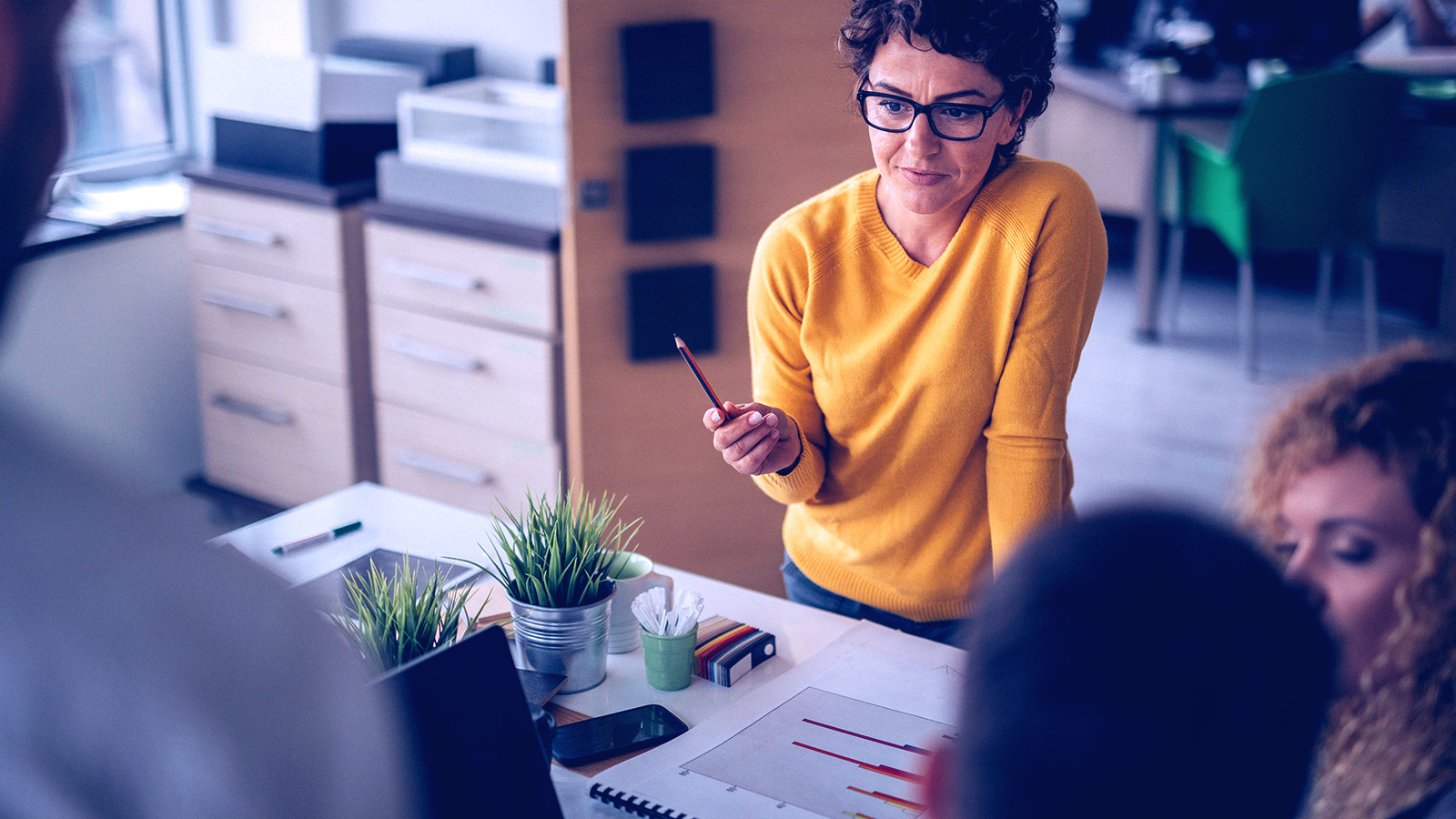 A women standing on the other side of the table presenting to a group. 