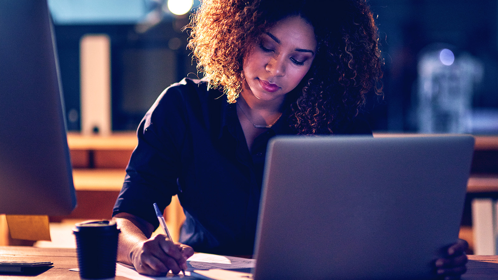 A women writing down notes in front of a laptop.