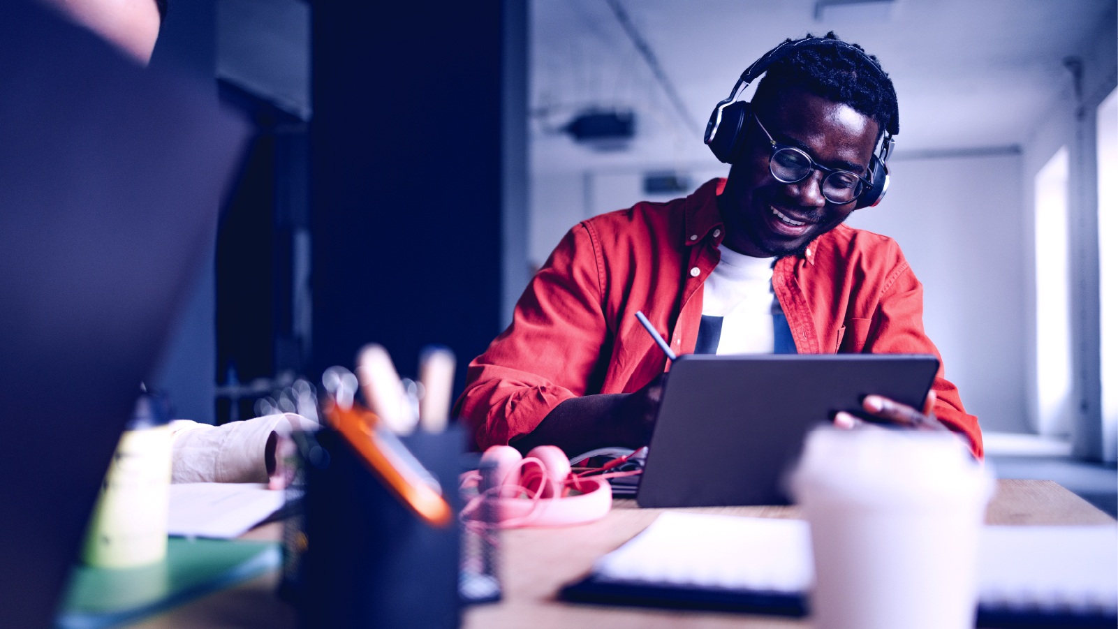 Student sitting at desk wearing headphones and listening to music while working on tablet