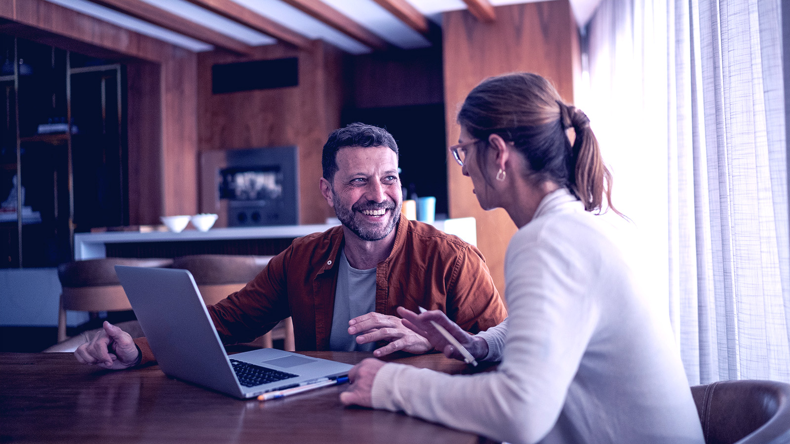 Coworkers in an office with wooden panelling sitting in front of a laptop dressed business casual