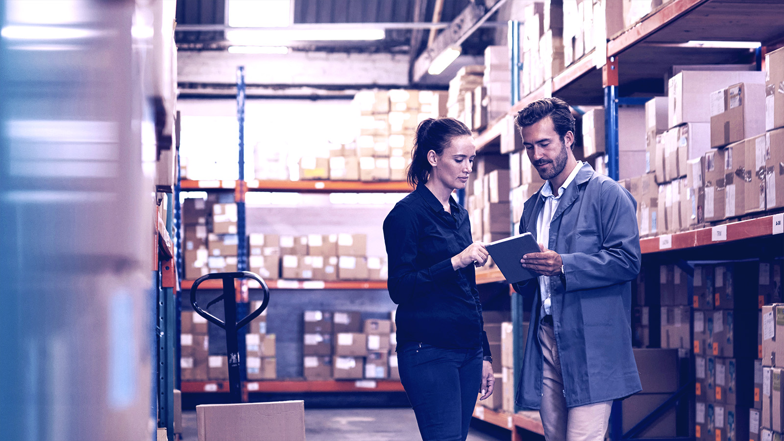 Coworkers discussing issues while standing in a warehouse holding a notepad