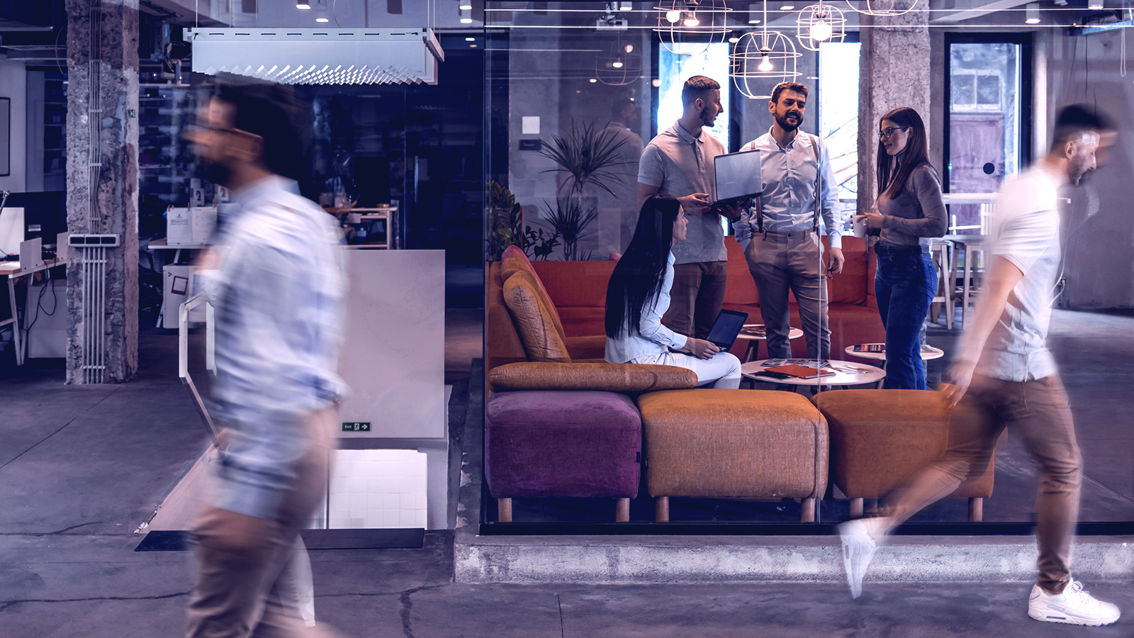 Two men walking outside a glass window with a group of team meeting inside