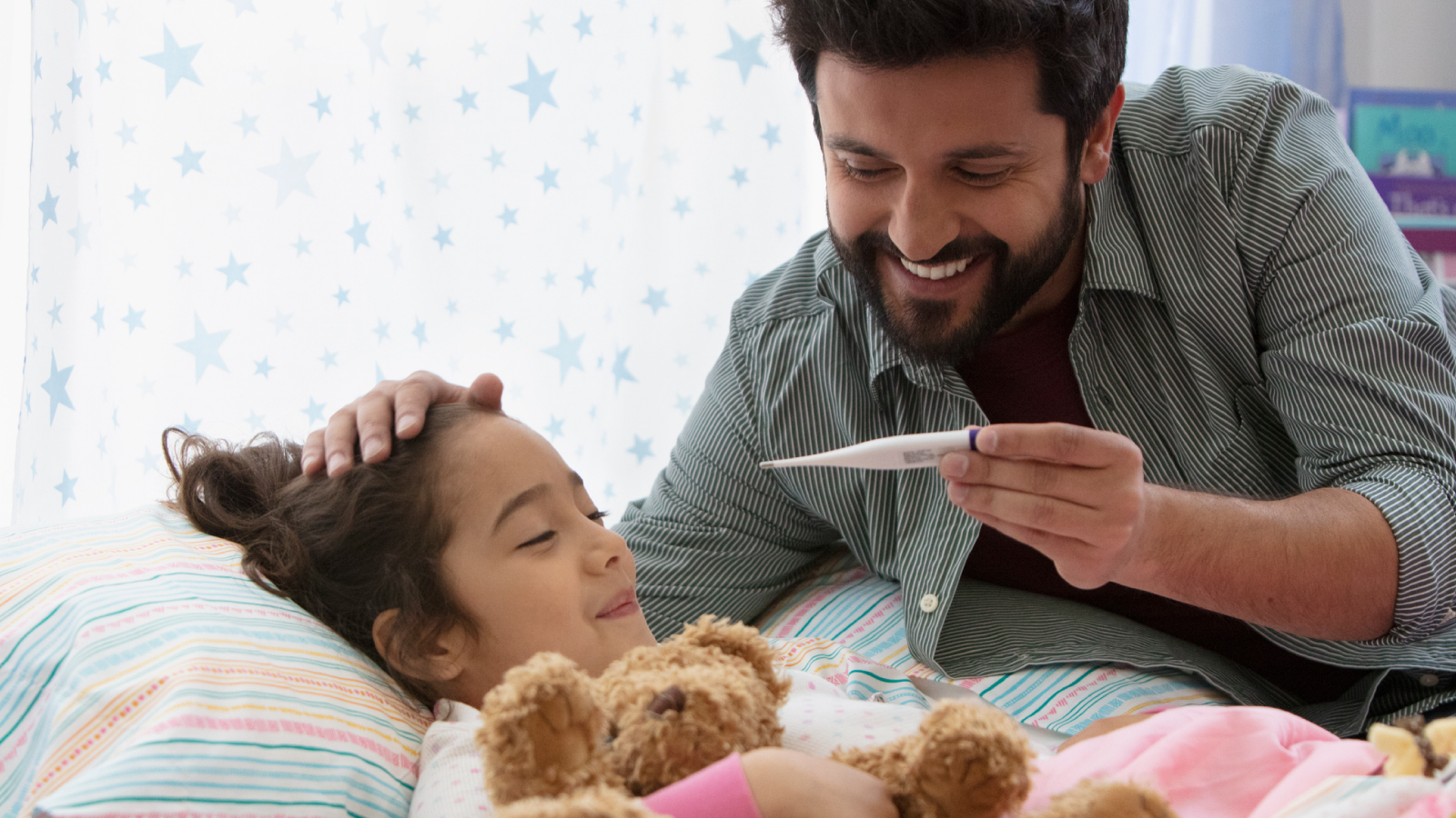 Dad rubbing daughters head while looking at a thermometer