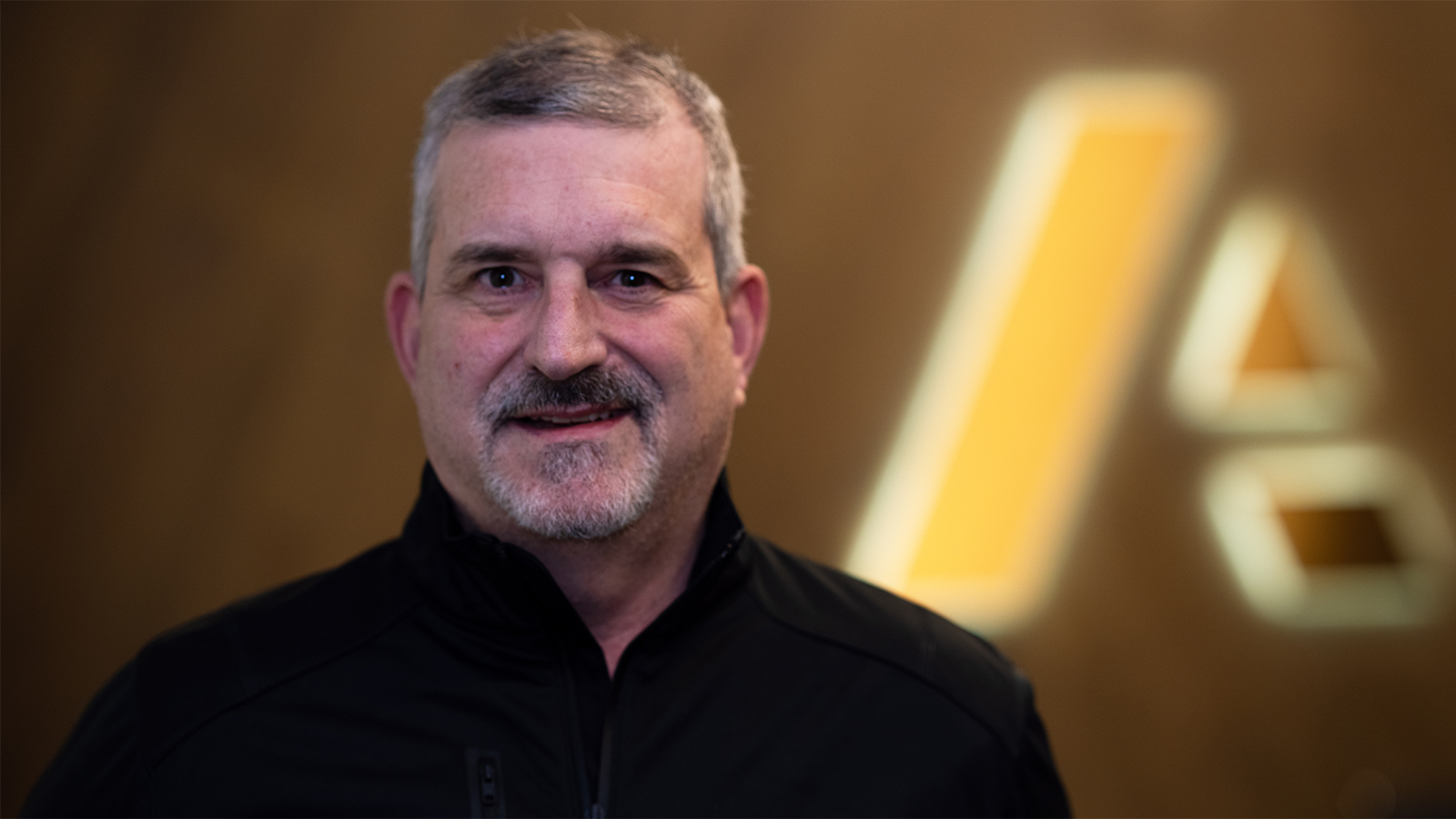 Adam Thier — businessman dressed in suit standing in front of Anaplan logo