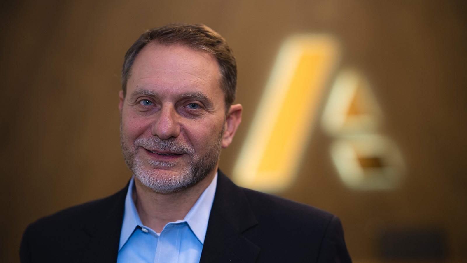 Greg Giangiordano — businessman dressed in suit standing in front of Anaplan logo